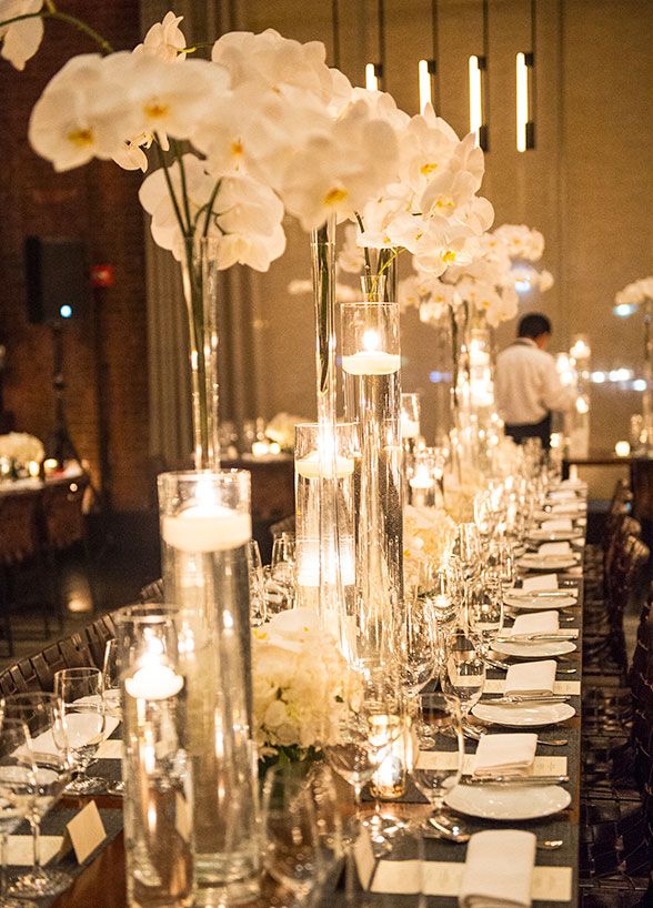 wedding table decor Tall glass vases are lush with white orchids and candles floating inside