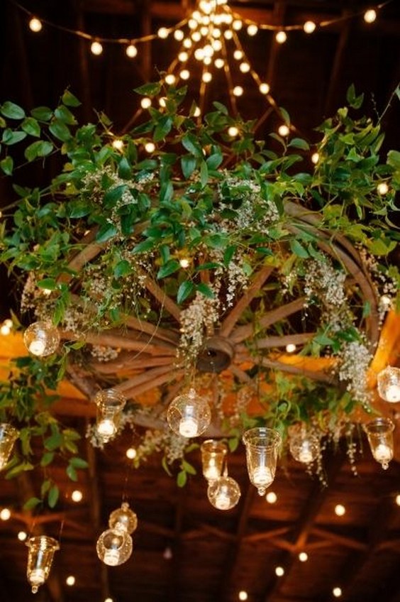 Wagon wheel-turned-floral chandelier with greenery and hanging votives