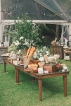 rustic bread, cheese, and charcuterie table decorated with a centerpiece of lush greenery and white peonies