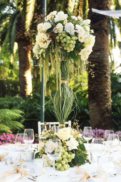 A tall centerpiece of roses and fresh green grapes is covered in grass