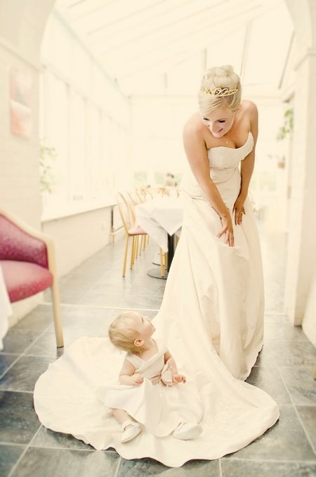 Bride looking down at baby flower girl sitting on floor