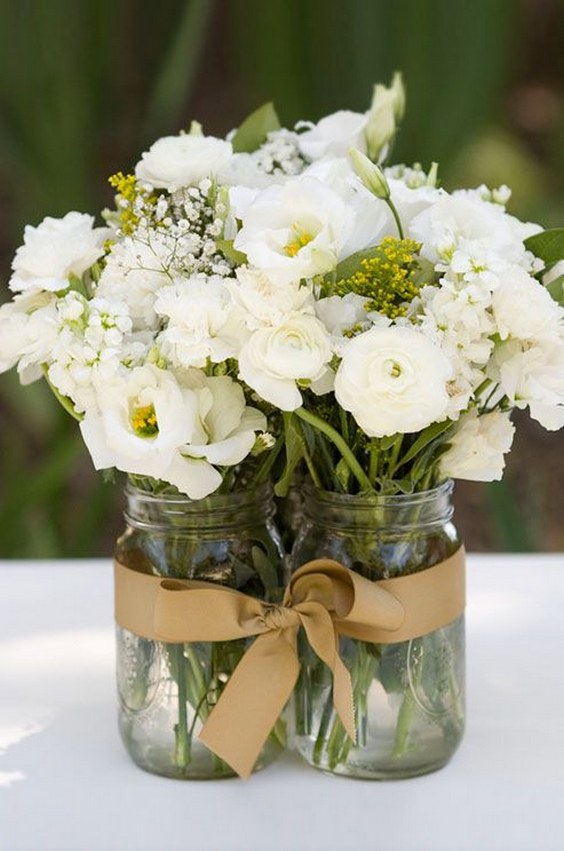 Mason jars are filled with white lisianthus and ranunculus flowers for a rustic fee