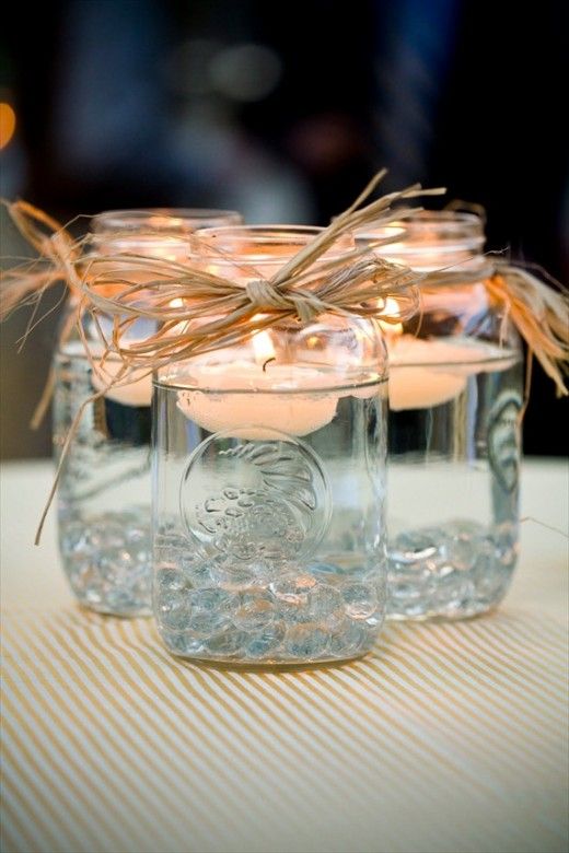 Mason jars filled with water and a decorative ribbon or string tied around the rim with a long burning floating candle in each jar