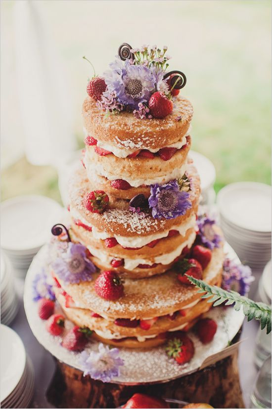 Naked wedding cake with powdered sugar, berries, and flowers