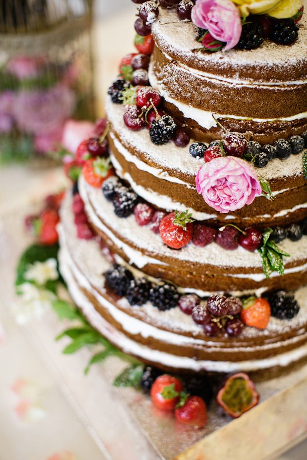 naked wedding cake with each layer covered in berries and dusted with icing sugar
