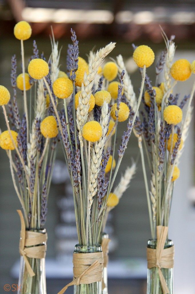 Wheat yellow billy balls and purple lavender in wine bottles as centerpieces