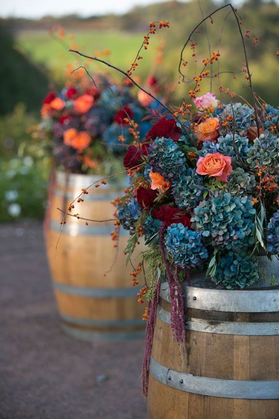 Blue hydrangea and branches atop wine barrels are the perfect winery wedding flower arrangement