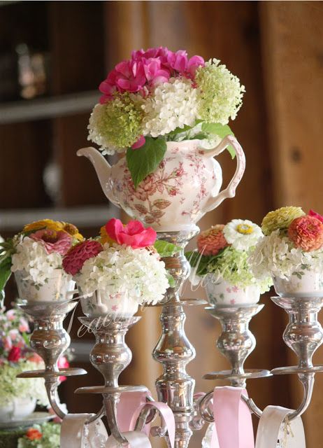 Fresh blooms in a teapot & cups decorate a silver candelabra