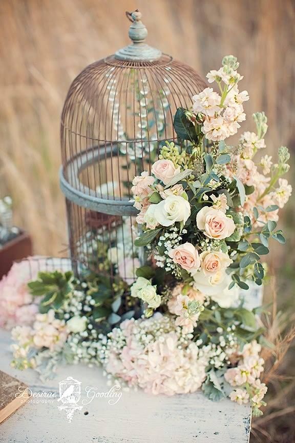 birdcage overflows with a gorgeous flower arrangement for rustic wedding