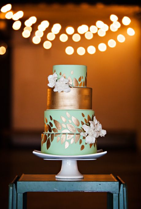 four-tiered mint-and-gold wedding cake with gold-leaf details and fresh flowers
