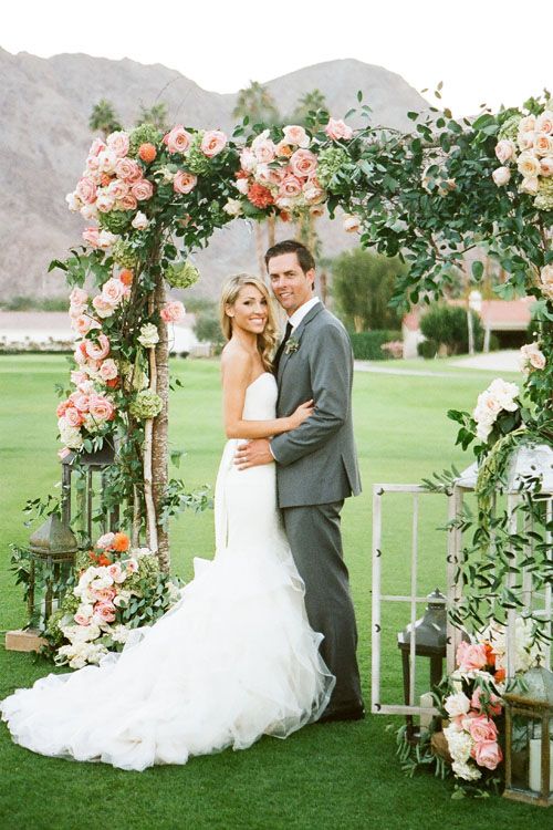 wedding ceremony arch covered with peach and coral flowers and lush greenery