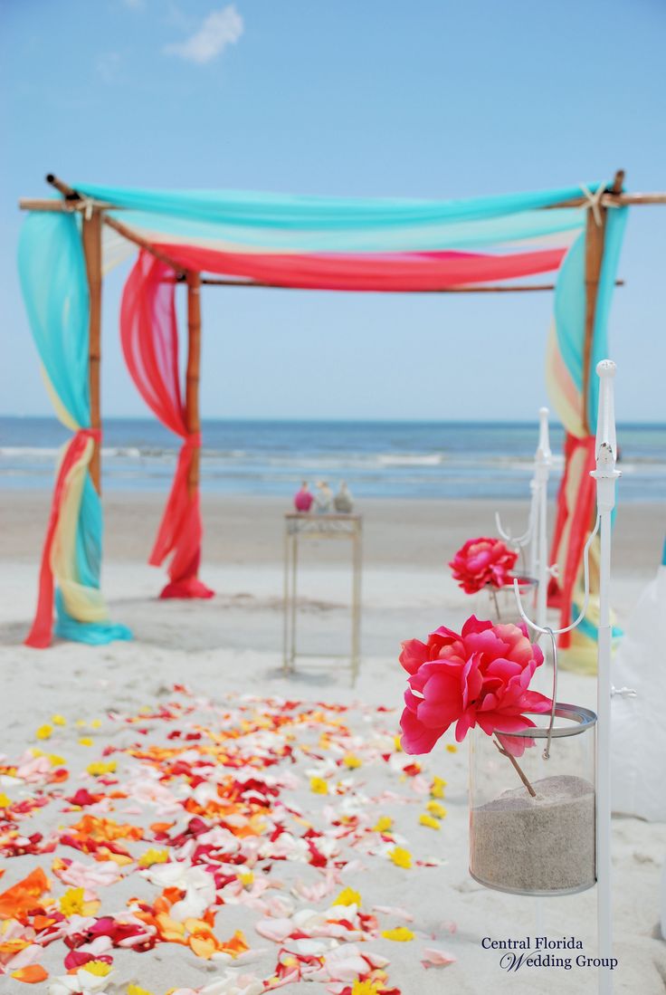 Tropical beach wedding, 4-post bamboo with turquoise, yellow, coral, and hot pink sheers, turquoise chair sashes, vases along the aisle, & flower petal aisle
