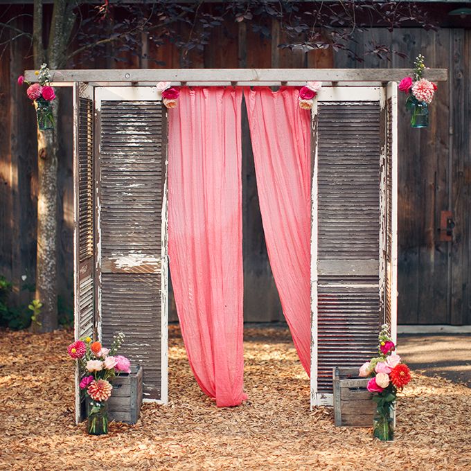 rustic wedding altar made of weathered shutters and gauzy pink fabric, complete with colorful flowers
