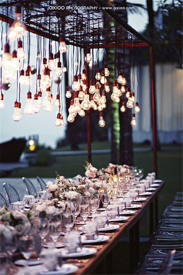 Edison bulbs hanging at different heights clustered over reception tables