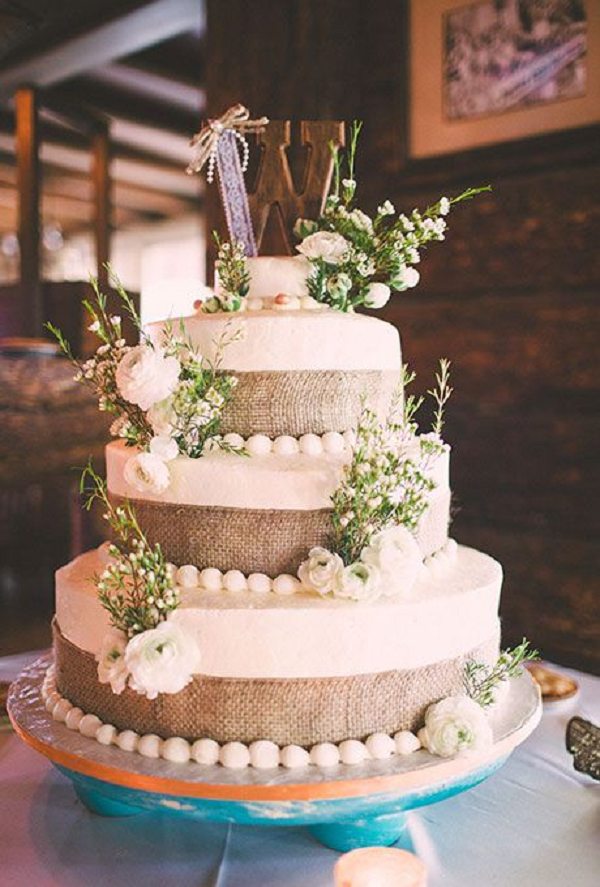 three-tiered wedding cake with burlap wrapped tiers, fresh white ranunculus, and greenery accents