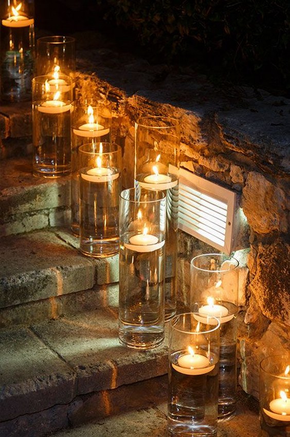 Single floating candles in narrow glass hurricanes illuminate stone steps for guests