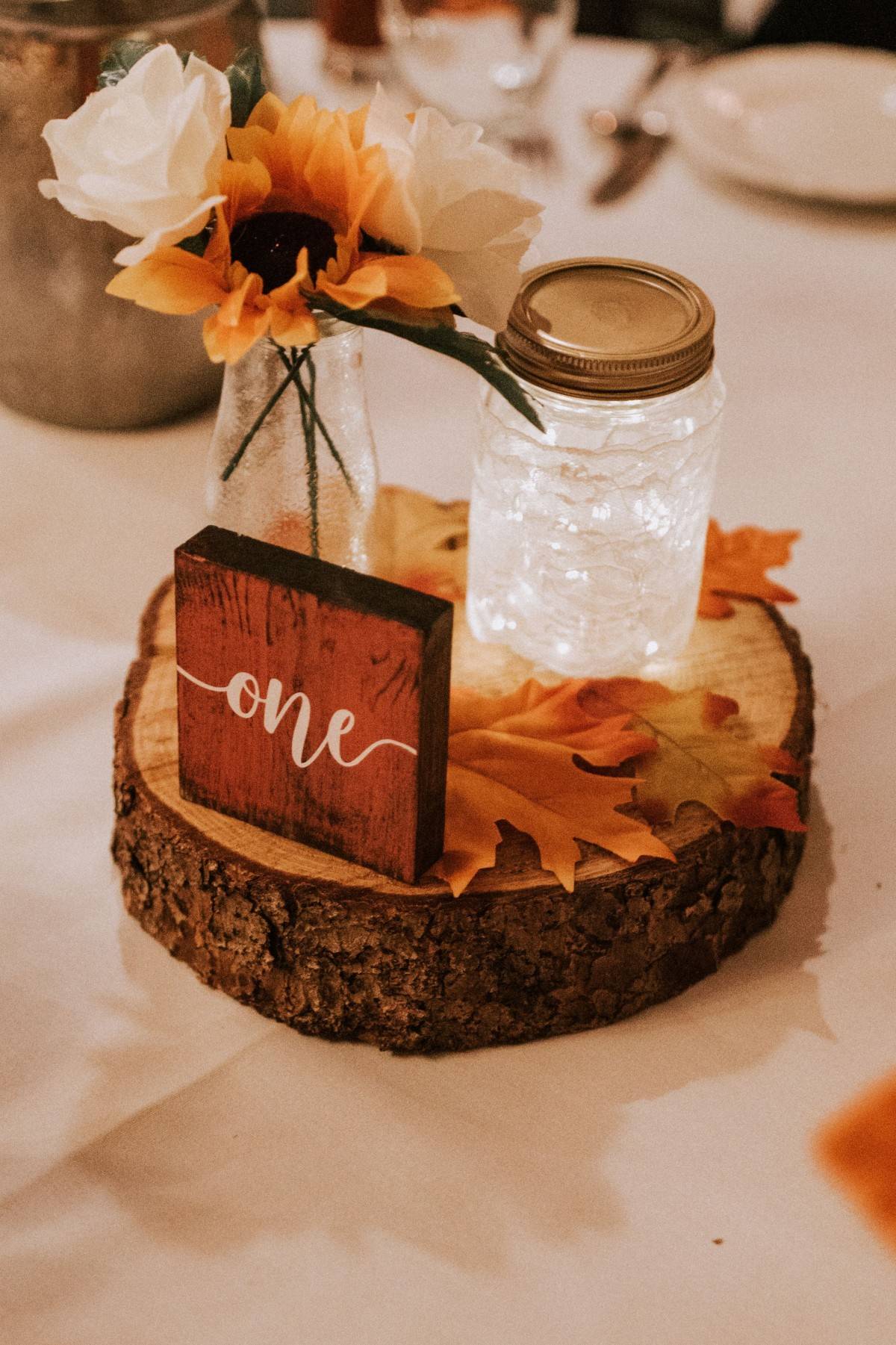 rustic fall mason jar with fairy lights and wood table number on tree stump centerpiece