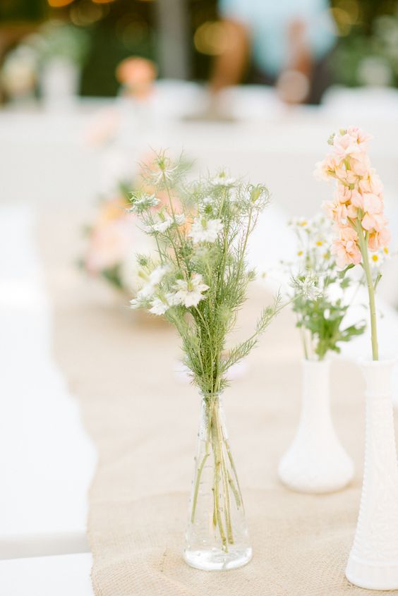 Antique milk glass bud vases of Nigella flowers, Stock flower and Chamomile on a burlap runner