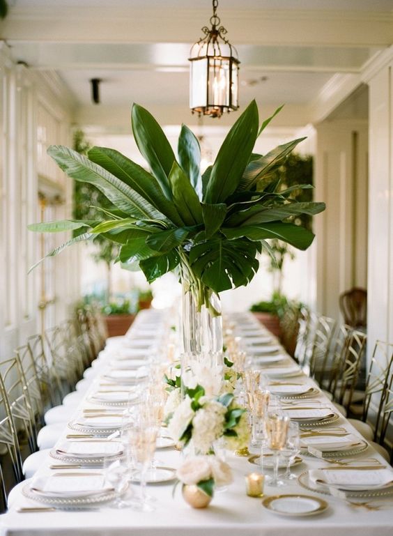 palm leaf wedding tablescape with gold tones in flatware guest chairs and place settings