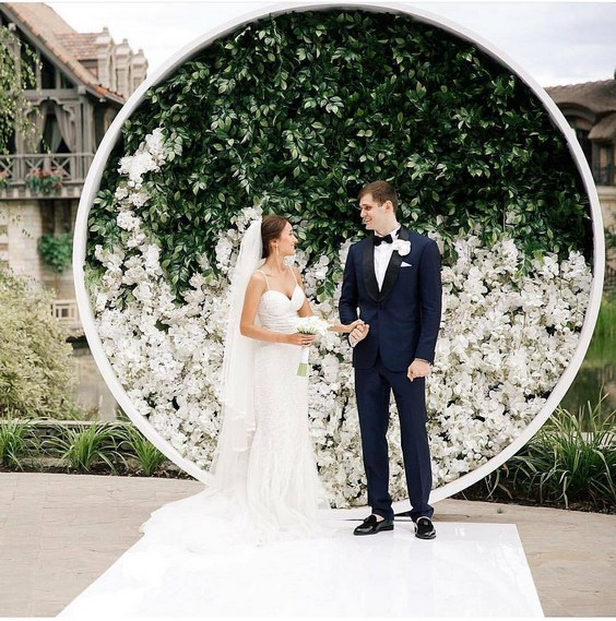 circular backdrop adorned with greenery and white hued bloom