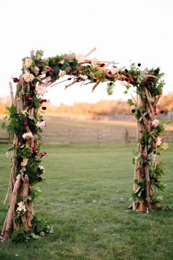 wood ceremony arch consisting of branches, greenery and jewel toned flowers