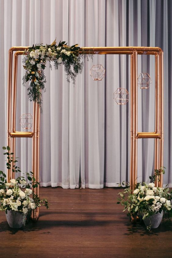 Industrial copper wedding ceremony arbour with florals in concrete pots