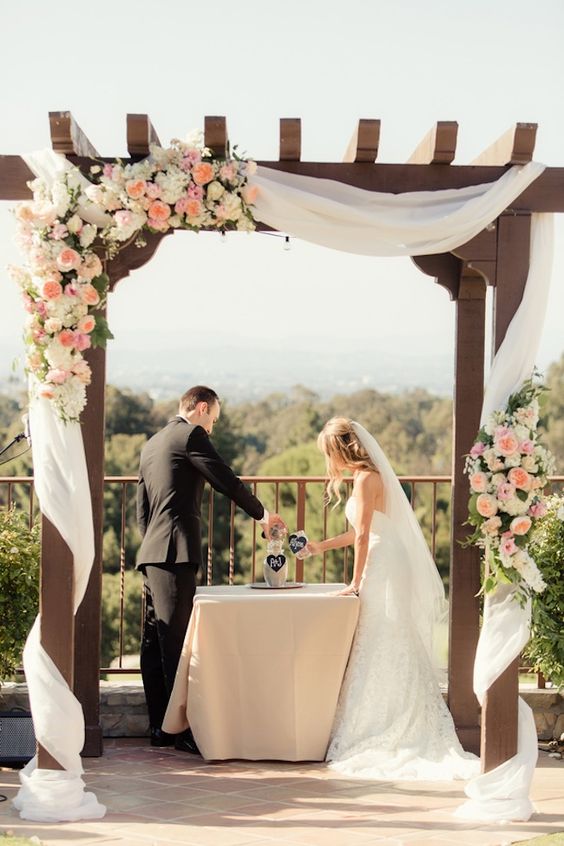 outdoor wedding arch draped with fabric and flurry of peach pink garden roses