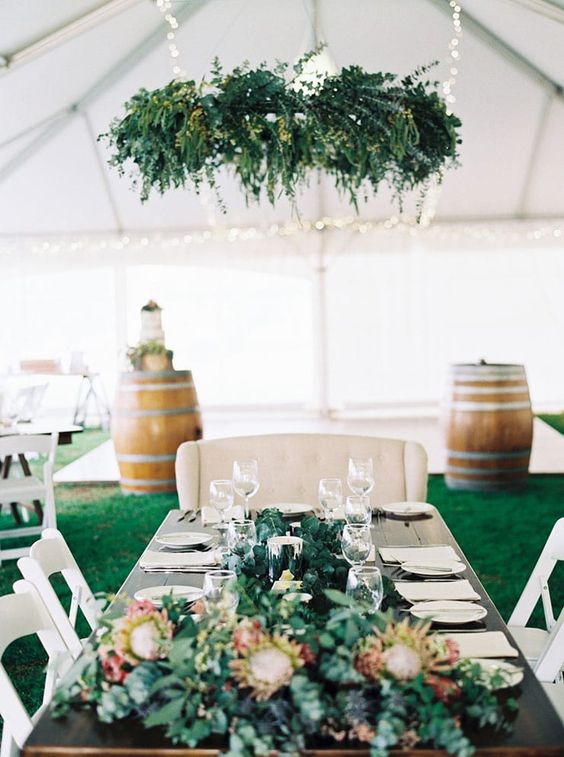 Rustic elegant wedding reception in a white marquee with greenery chandelier and protea bridal table arrangement