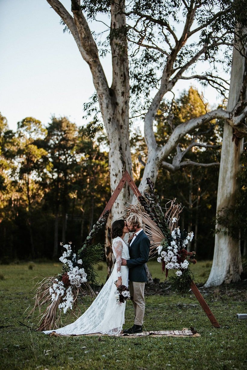 Rustic boho outdoor wedding ceremony with triangle arch, dried palms and white roses