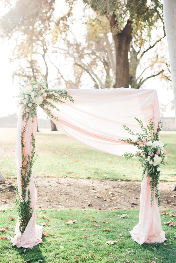 blush pink wedding ceremony altar with draped fabric and greenery