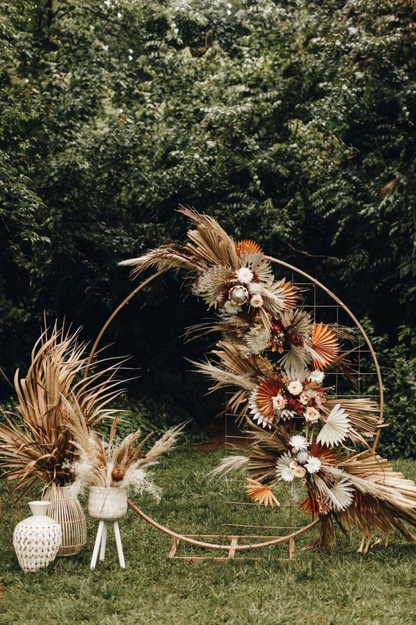 Gorgeous fall-inspired ceremony decor featuring a circular backdrop decked with dried palms + warm toned florals