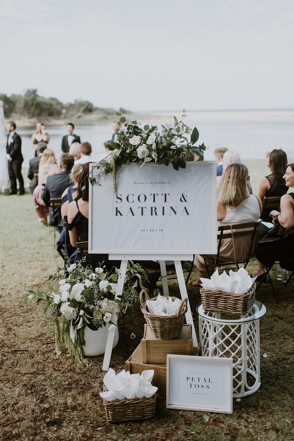 Modern romantic beach wedding ceremony welcome sign with green and white flowers and petal cones