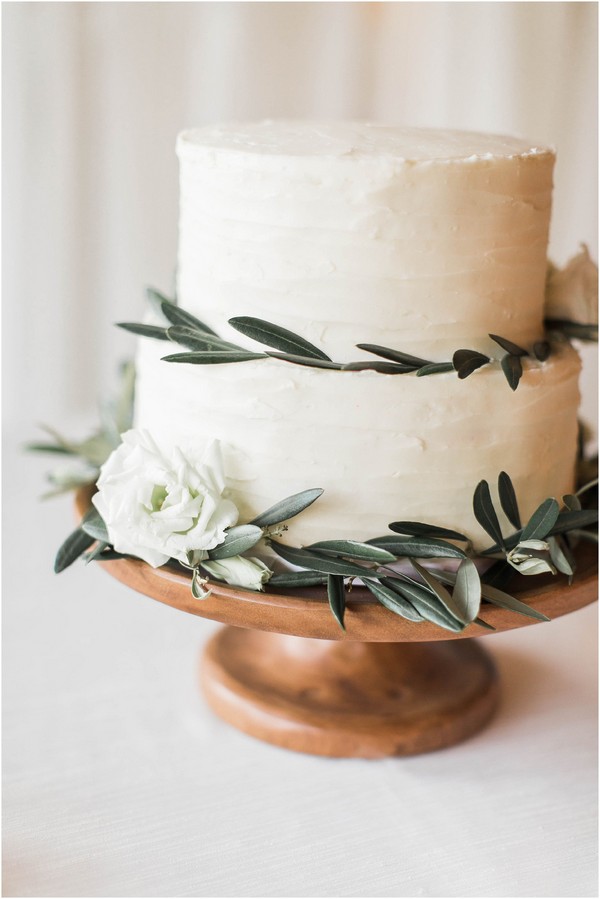 Simple Elegant Wedding Cake with Olive Leaves and White Flowers on a Wooden Cake Stand