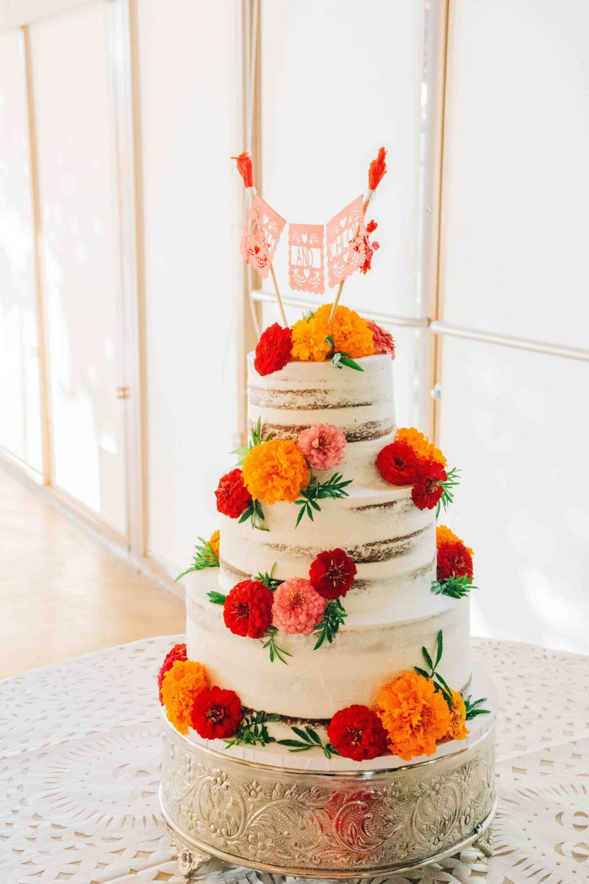 3 tier rustic semi-naked wedding cake with red and orange flowers and mexican cake topper