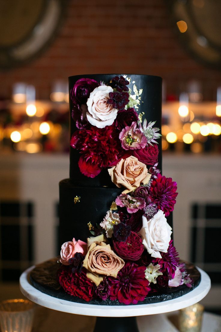 black two tier wedding cake with burgundy dahlias and orange roses
