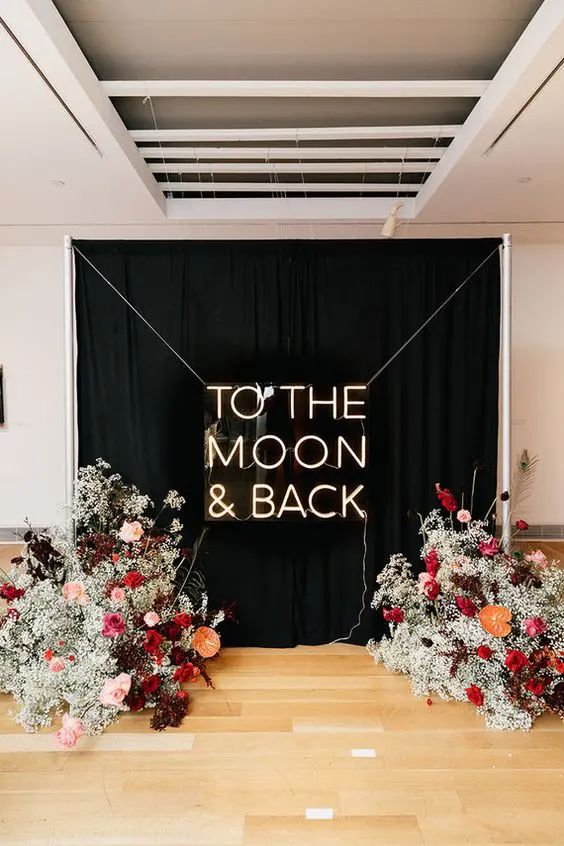 modern wedding ceremony space wiht a black and neon backdrop, with baby's breath, pink, red, burgundy blooms