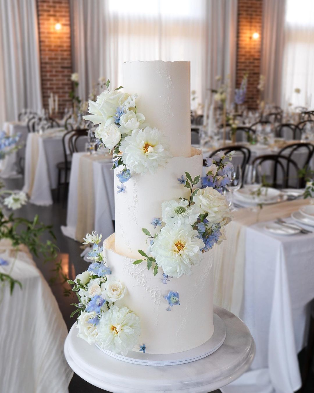 elegant white wedding cake with blue flowers via milkandhoney.cakecreative