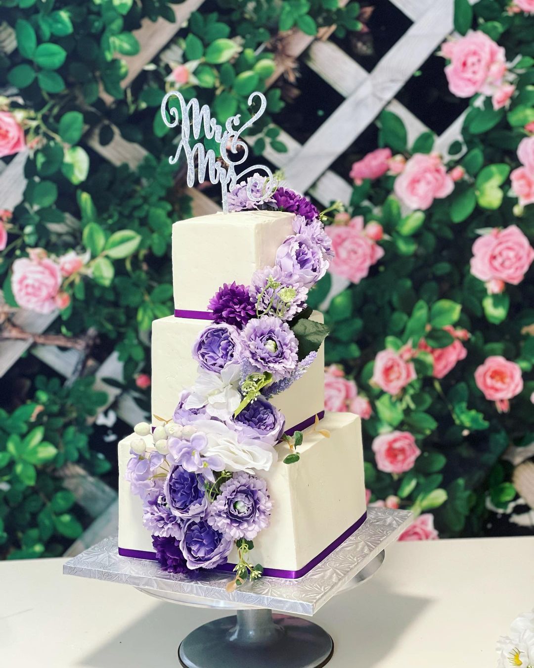 3 tier square wedding cake with purple artificial flowers via cakebusters416